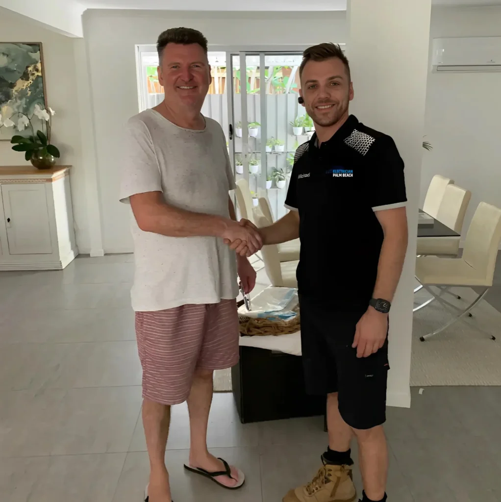 Two men shaking hands in a modern home, one in casual clothes holding keys, the other in a work uniform with boots, both smiling.